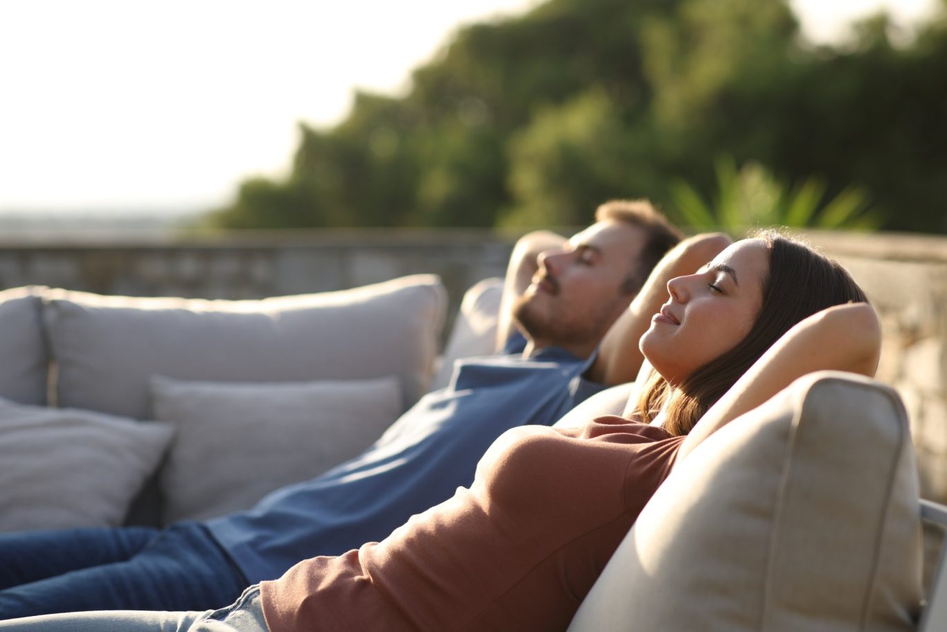 Relaxed couple sitting on outdoor furniture on a terrace.