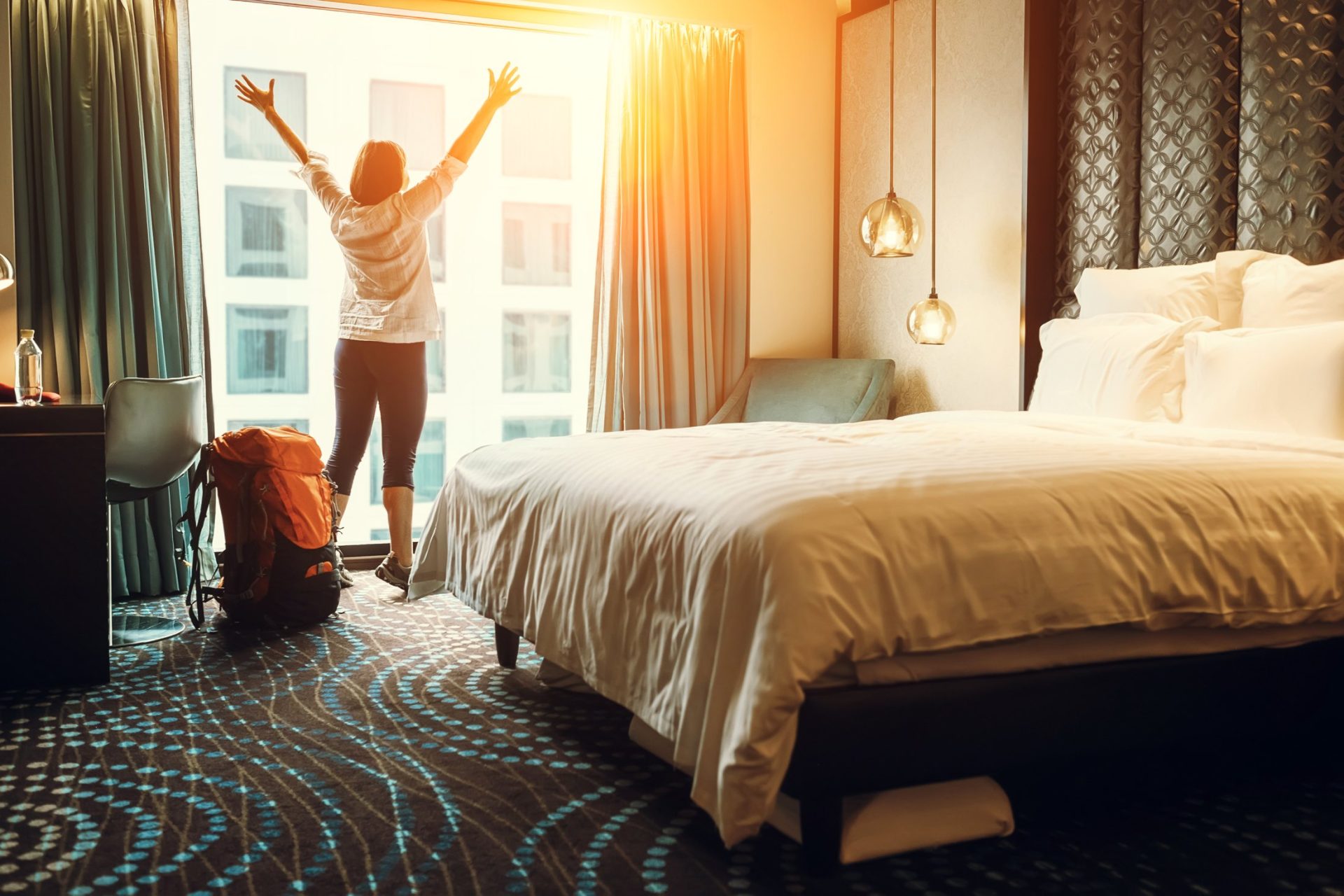 Traveler stretching with joy in modern hotel room at sunrise.