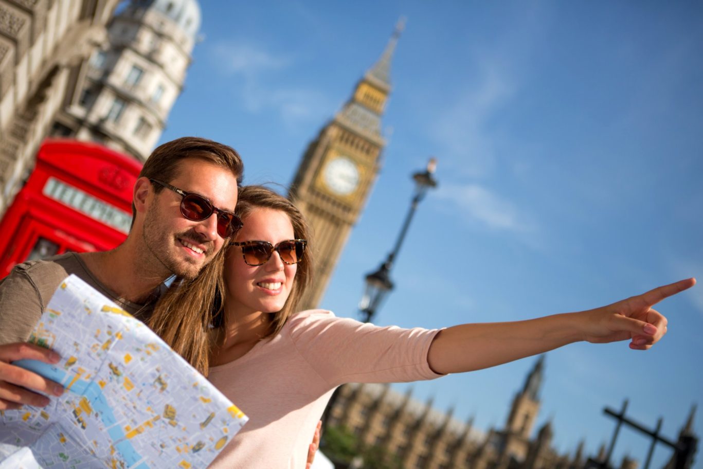 Happy tourists with a city map sightseeing in London near Big Ben and a red telephone booth.