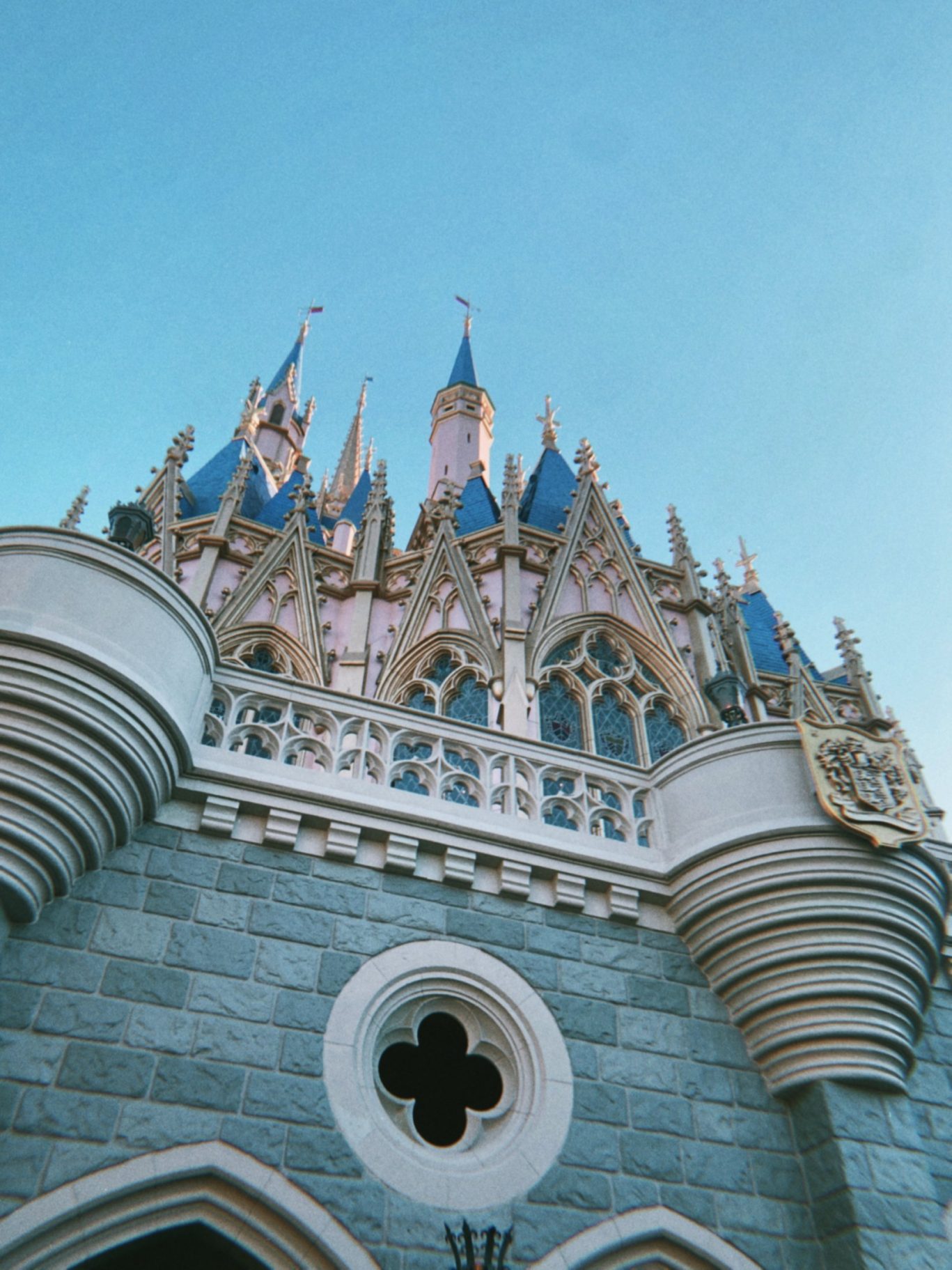 Upward view of a whimsical fairytale castle with blue spires and ornate details against a blue sky.