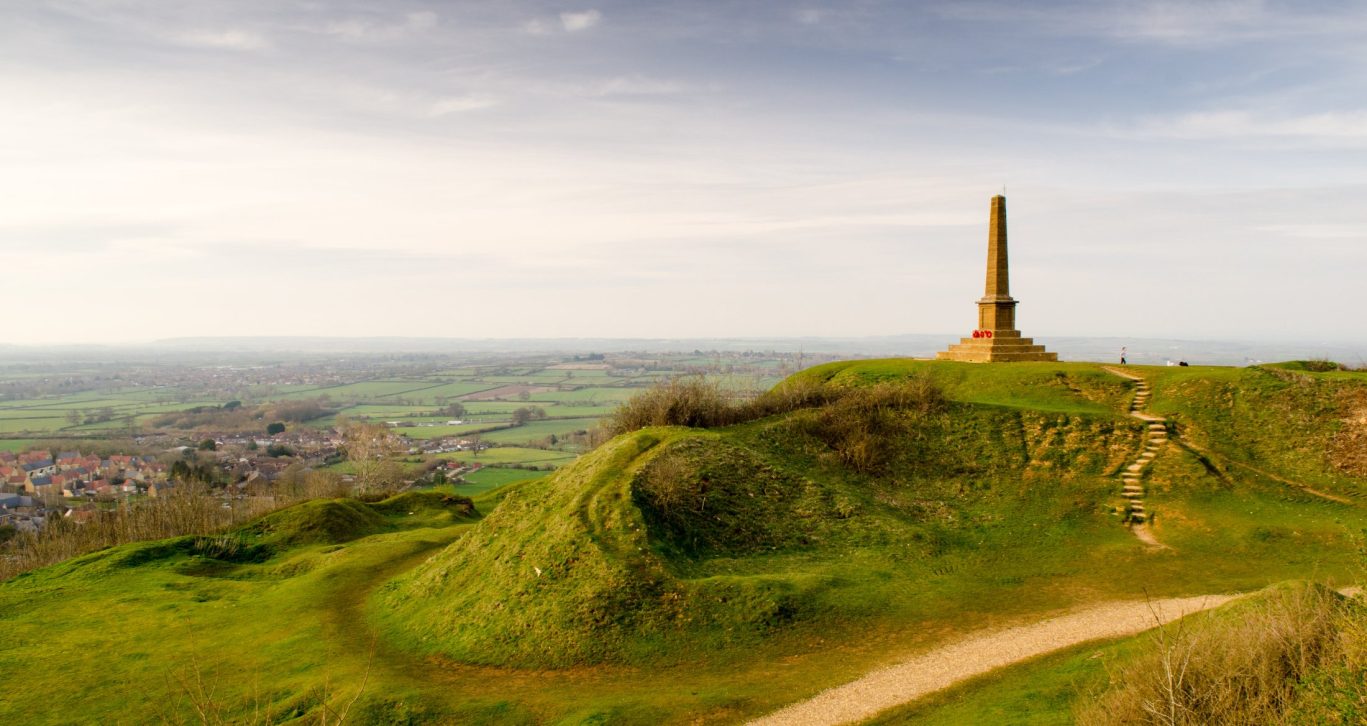 Panoramic view from King Alfred’s Tower in Somerset with lush green hills and a countryside village below.